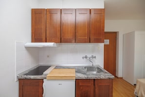 A kitchen with wooden cabinets, a stainless steel sink, a white dishwasher, and a marble countertop. - Charming Studio Retreat in Malinska-Dubašnica with Garden View (Malinska-Dubašnica)