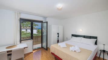 Habitación de hotel con cama, escritorio, silla, balcón con vistas y puerta que da a otra habitación.