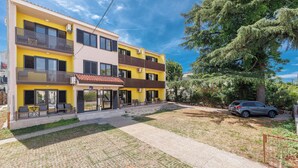 A multi-story building with balconies, a paved driveway, and a car parked in the driveway. - Charming Studio in Malinska close to the beach (Malinska-Dubašnica)