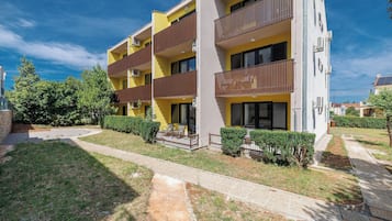 Un edificio residencial de varios pisos con balcones, un camino de entrada pavimentado y jardines bien cuidados.