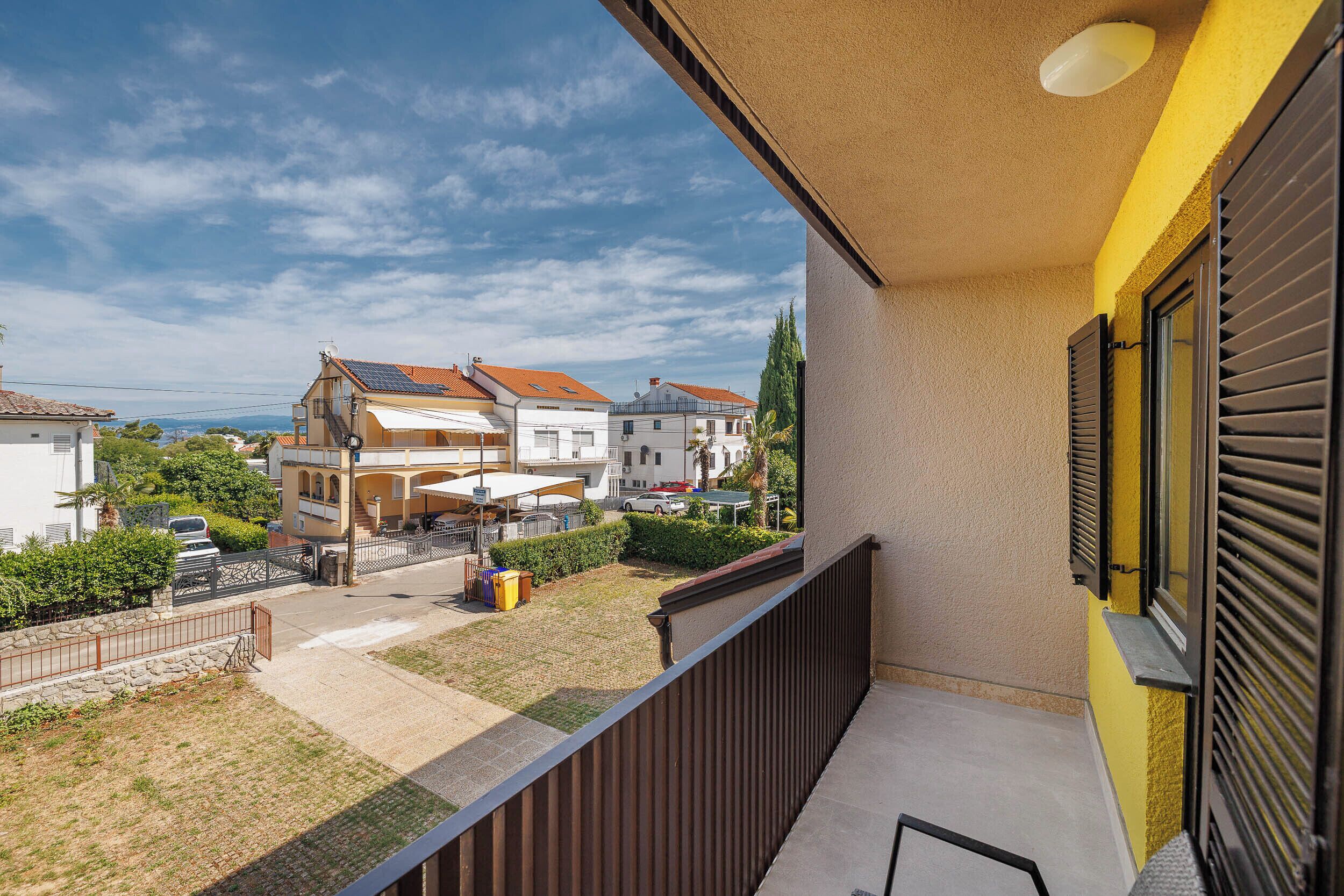 Un balcón con vista a una zona residencial, que incluye casas y un cielo despejado.