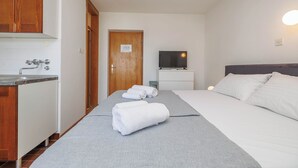 A hotel room with a bed, a TV, a small table, and a kitchenette. - Charming Studio in Malinska close to the beach (Malinska-Dubašnica)