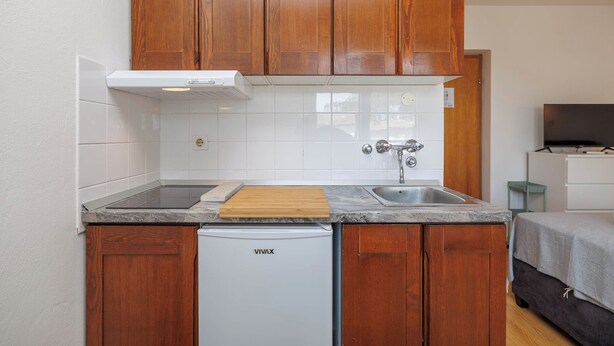 A compact kitchen with wooden cabinets, a built-in dishwasher, and a small countertop. - Charming Studio in Malinska close to the beach (Malinska-Dubašnica)
