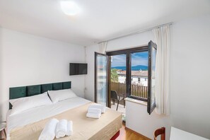 A hotel room with a bed, a TV, a balcony with a view, and a chair. - Charming Studio Rental in Malinska with Garden View (Malinska-Dubašnica)