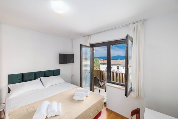 Habitació d'hotel amb llit, televisió, balcó amb vistes i una cadira.