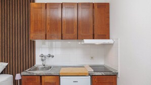 A compact kitchen with wooden cabinets, a built-in dishwasher, and a countertop with a cutting board. - Charming Studio Rental in Malinska with Garden View (Malinska-Dubašnica)