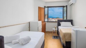 A hotel room with two beds, a small table, a window with a view, and an air conditioning unit. - Charming Studio Rental in Malinska with Garden View (Malinska-Dubašnica)