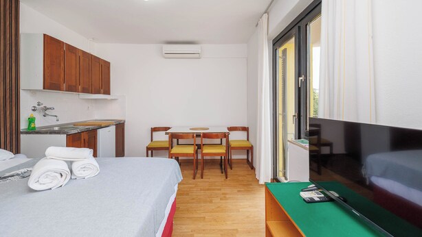 A compact hotel room with a bed, a small kitchenette, a dining table with chairs, a TV, and a sliding glass door. - Charming Studio for 4 persons in Malinska (Malinska-Dubašnica)