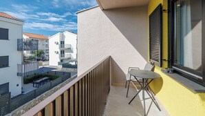 A balcony with a table and chairs, a window with shutters, and a view of neighboring buildings. - Charming Studio for 4 persons in Malinska (Malinska-Dubašnica)