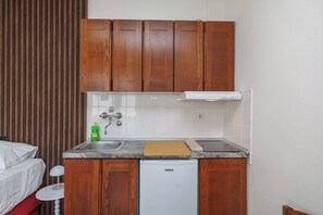 A compact kitchenette with wooden cabinets, a white dishwasher, a sink with a faucet, and a countertop with a cutting board and dish soap. - Charming Studio for 4 persons in Malinska (Malinska-Dubašnica)