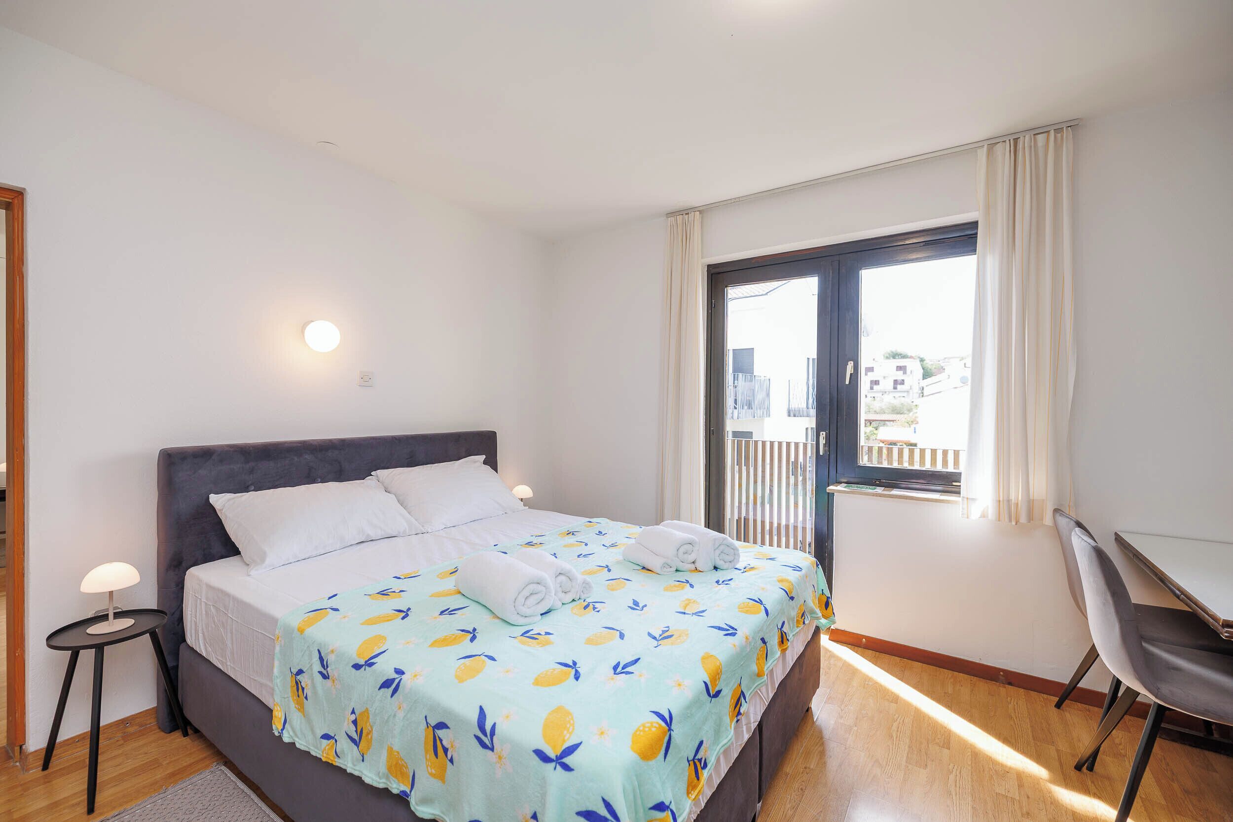 Ein Schlafzimmer mit Bett, Schreibtisch, Stuhl, Fenster und einem Balkon.