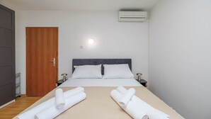 Habitación de hotel con una cama, dos mesitas de noche, una puerta de madera y un equipo de aire acondicionado.