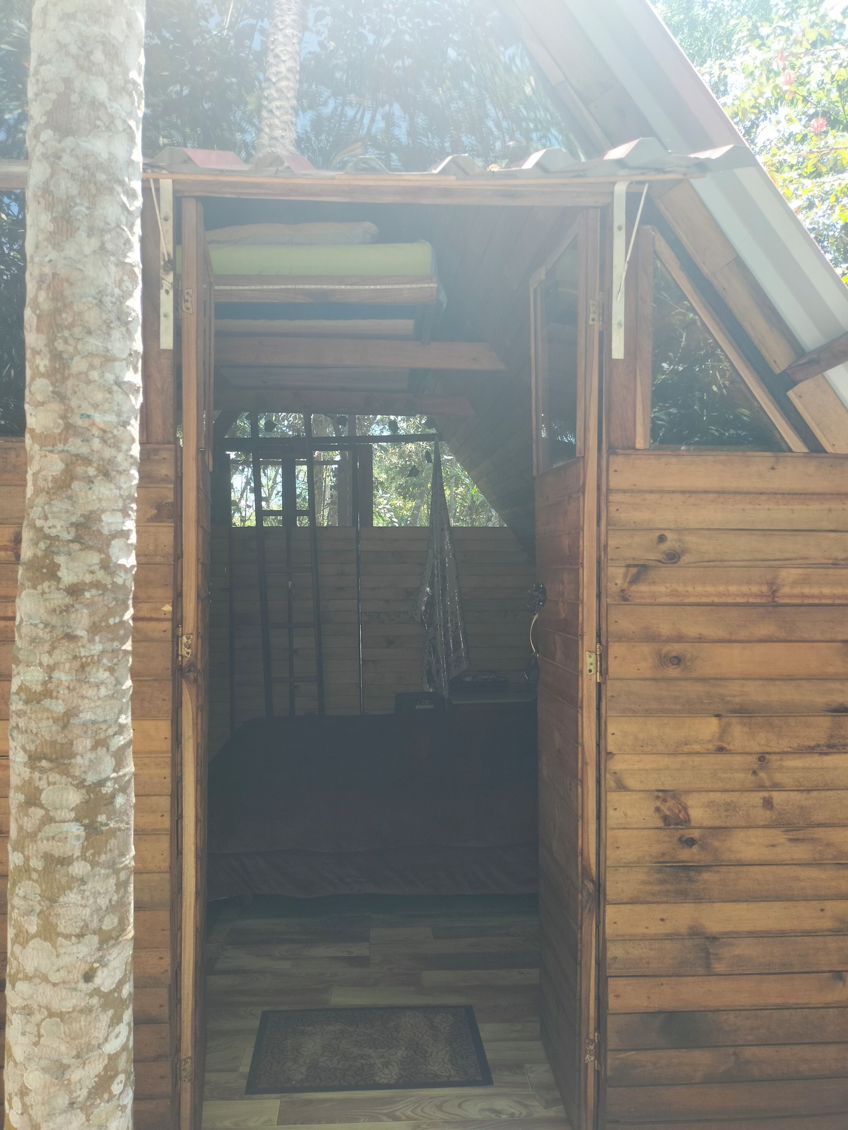 Una puerta de madera abierta que da a una habitación con suelo de madera, una escalera y una ventana.