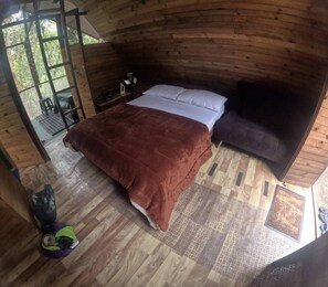 Une chambre dans une cabane en bois, avec un lit, une table de chevet et une fenêtre donnant sur la verdure.