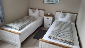 A bedroom with two single beds, a nightstand, a framed picture on the wall, and a window with curtains. - 5 - Schröder Apartment - Comfortable vacation rental in Zingst with a terrace and garden (Zingst)