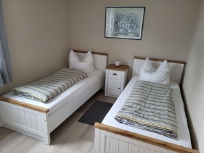 Ein Schlafzimmer mit zwei Einzelbetten, einem Nachttisch, einem gerahmten Bild an der Wand und einem Fenster mit Vorhängen.
