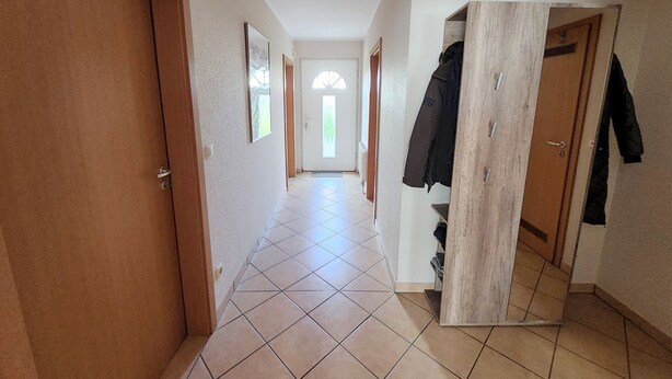A hallway with tiled flooring, wooden doors, and a coat rack. - 5 - Schröder Apartment - Comfortable vacation rental in Zingst with a terrace and garden (Zingst)