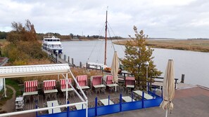 En restaurant ved floden med udendørs siddepladser, en båd i baggrunden og udsigt over floden.