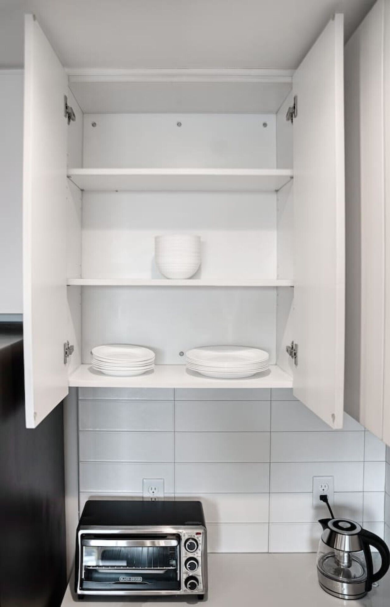 A kitchen with a built-in oven, a kettle, and a cabinet with shelves.