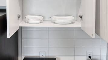 A kitchen with a built-in oven, a kettle, and a cabinet with shelves.