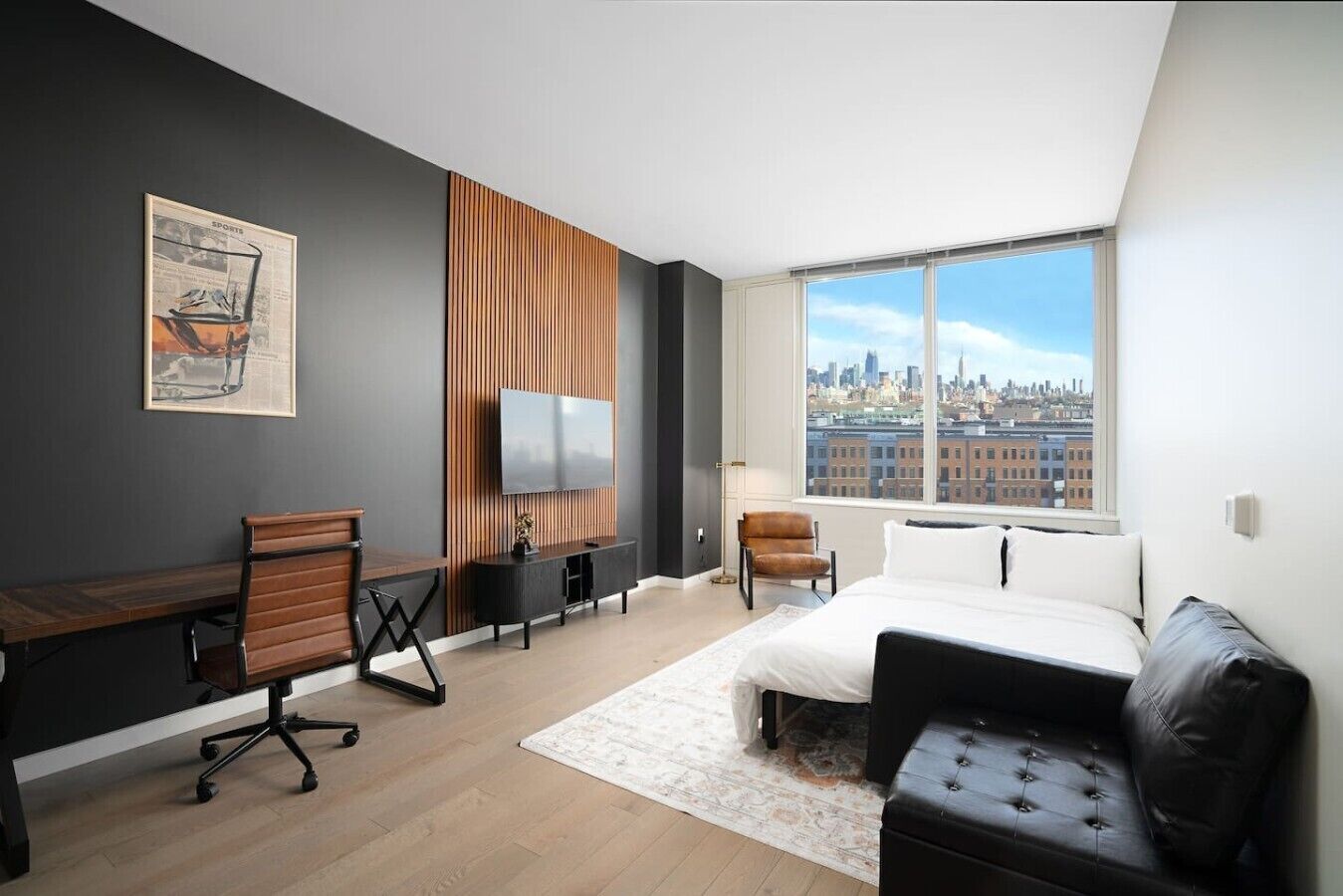 A modern hotel room with a large window, a desk, a bed, and a seating area.
