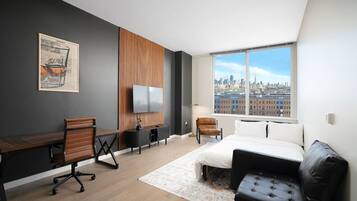 A modern hotel room with a large window, a desk, a bed, and a seating area.