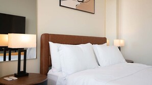 Quarto de hotel com uma cama, duas luminárias de cabeceira, uma mesa de cabeceira com controle remoto e uma obra de arte pendurada na parede.