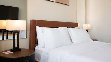 A hotel room with a bed, two bedside lamps, a nightstand with a remote control, and a wall-mounted artwork.