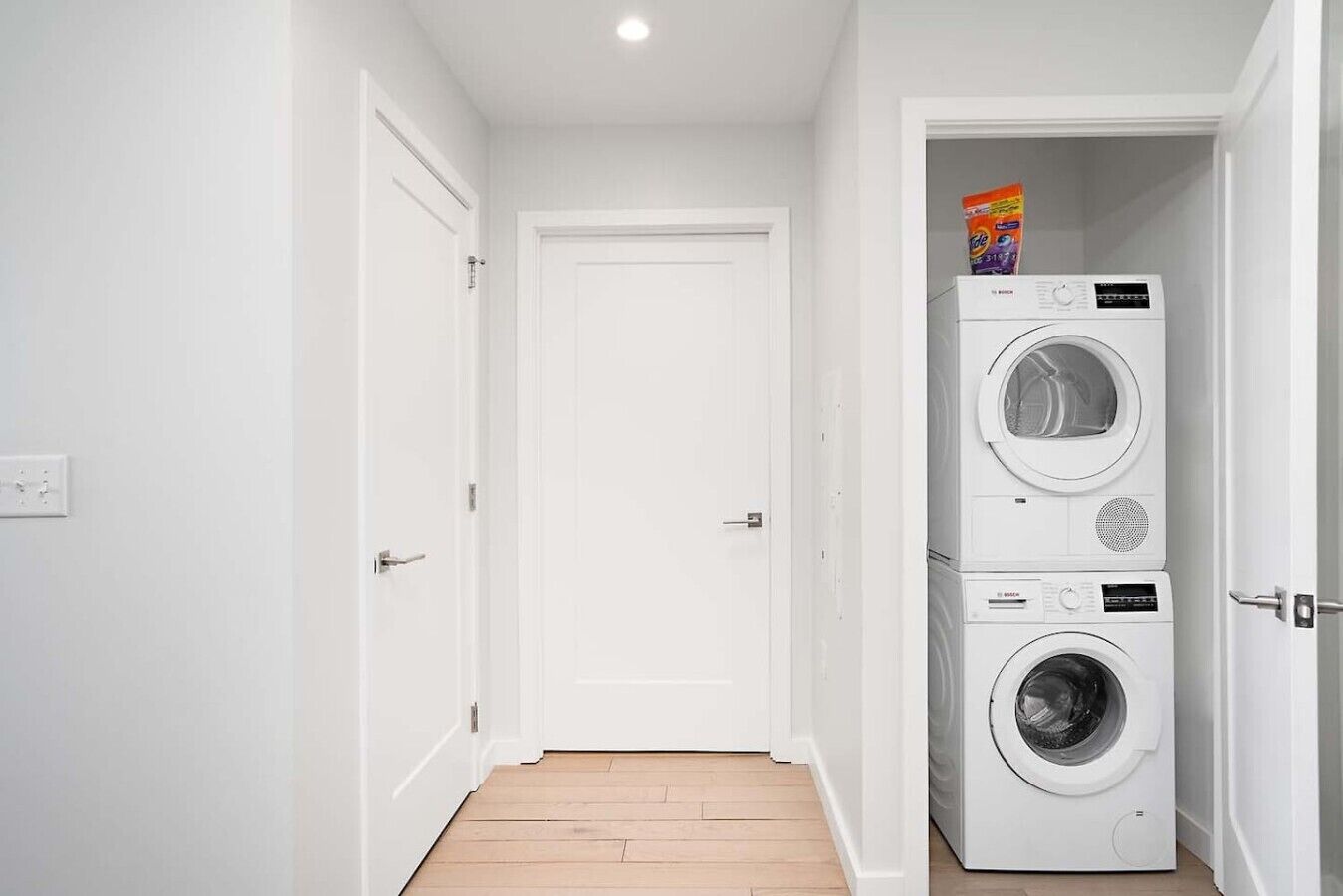 A laundry room with two stacked washing machines and a door leading to another room.