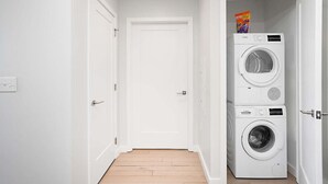 Uma lavanderia com duas máquinas de lavar empilhadas e uma porta que dá para outro cômodo.