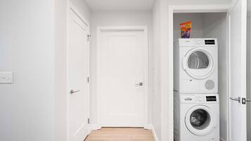 A laundry room with two stacked washing machines and a door leading to another room.