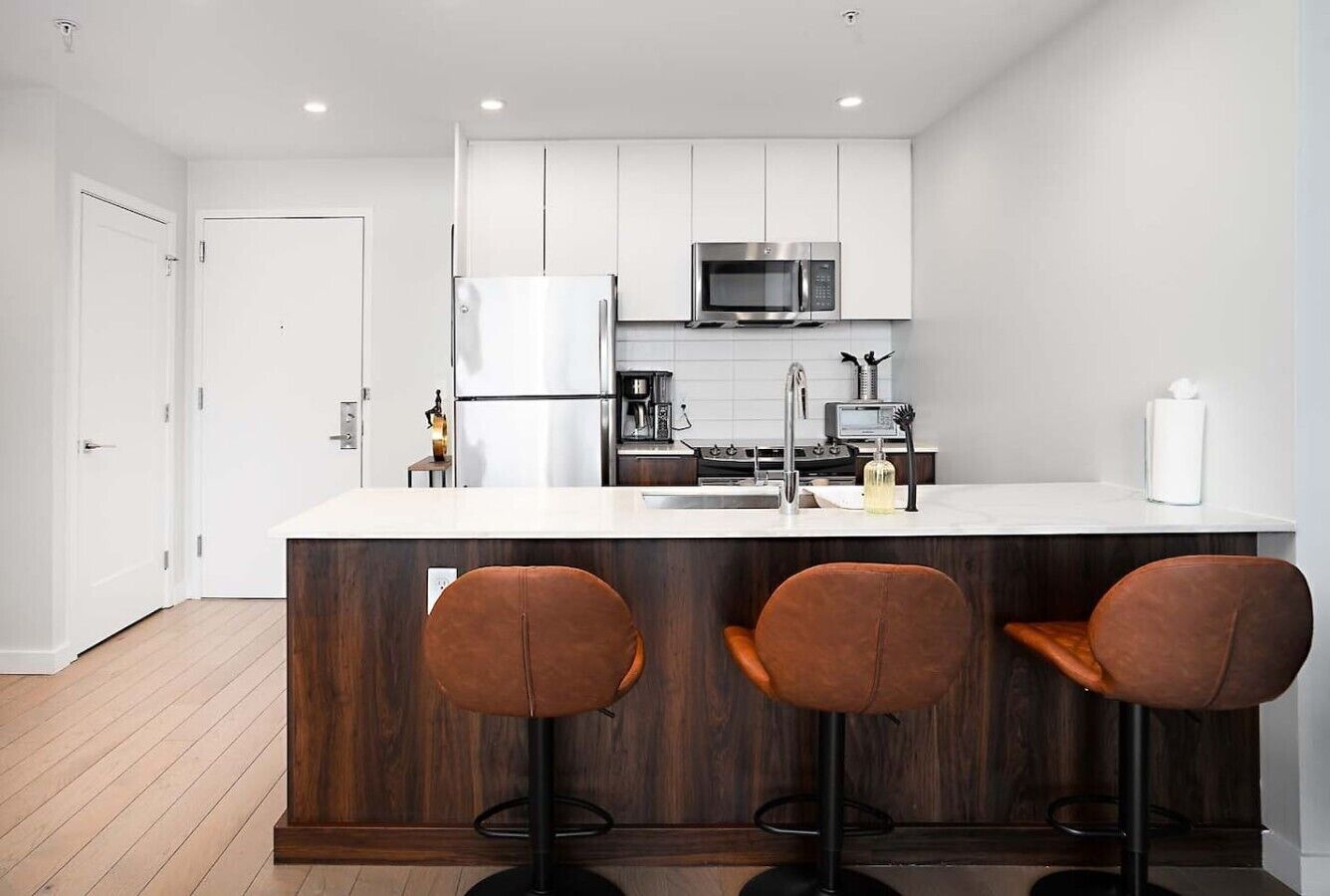 A modern kitchen with white cabinets, a stainless steel refrigerator, a microwave, and a wooden island with bar stools.