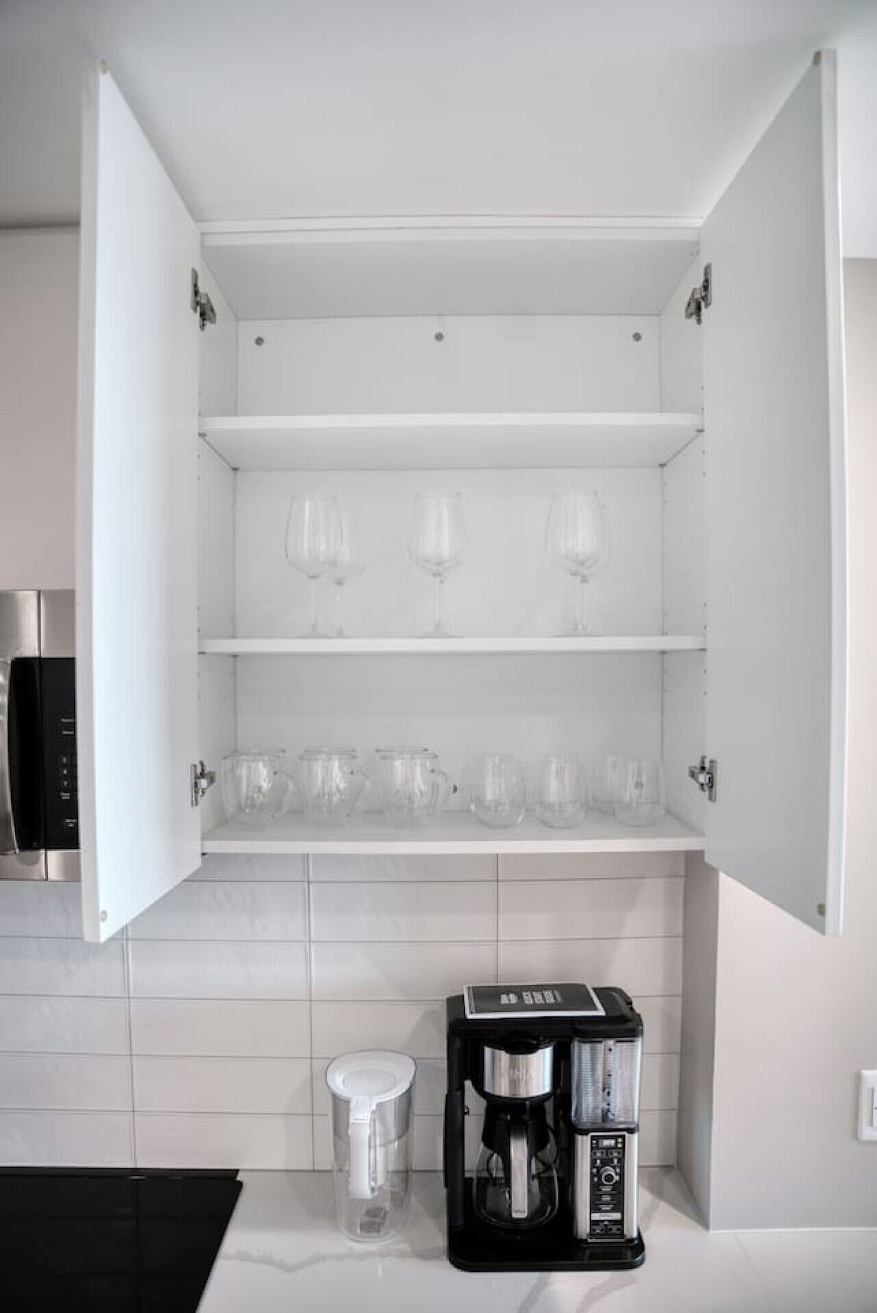A kitchen with a built-in cabinet, a coffee maker, and a trash bin.