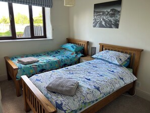 Une chambre à coucher avec deux lits en bois, chacun recouvert d’une couvre-lit à motifs de poissons bleus et blancs.