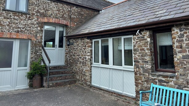 A stone building with a white door, a set of stairs leading to a porch, and a blue bench. - Granary @ Ivyleaf Barton, 3 bedroom cottage overlooking golf course to the sea (Bude)