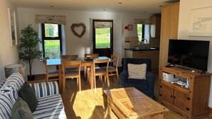 A living room with a sofa, a coffee table, a TV, and a kitchen area in the background. - Granary @ Ivyleaf Barton, 3 bedroom cottage overlooking golf course to the sea (Bude)