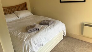 A neatly made bed with white linens and two folded towels, a wooden headboard, and a framed floral artwork on the wall. - Granary @ Ivyleaf Barton, 3 bedroom cottage overlooking golf course to the sea (Bude)