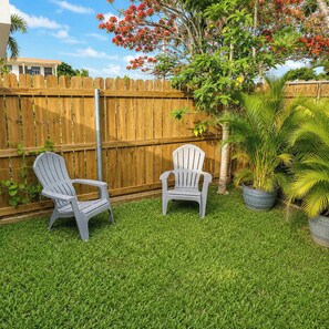 Ein Garten mit zwei Adirondack-Stühlen, einem Holzzaun und Topfpflanzen.
