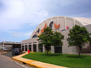 Ein modernes Gebäude mit einer gewölbten Fassade, einem Parkplatz und einem Schild mit der Aufschrift 'Aeropuerto Rafael Hernandez'.