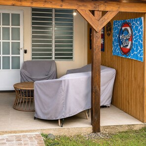 A covered outdoor seating area with a table and chairs, a wooden post, a door with glass panels, and a wall with a 'Puerto Rico' sign. - Los Flamboyanes Cozy Suite (Aguadilla city)