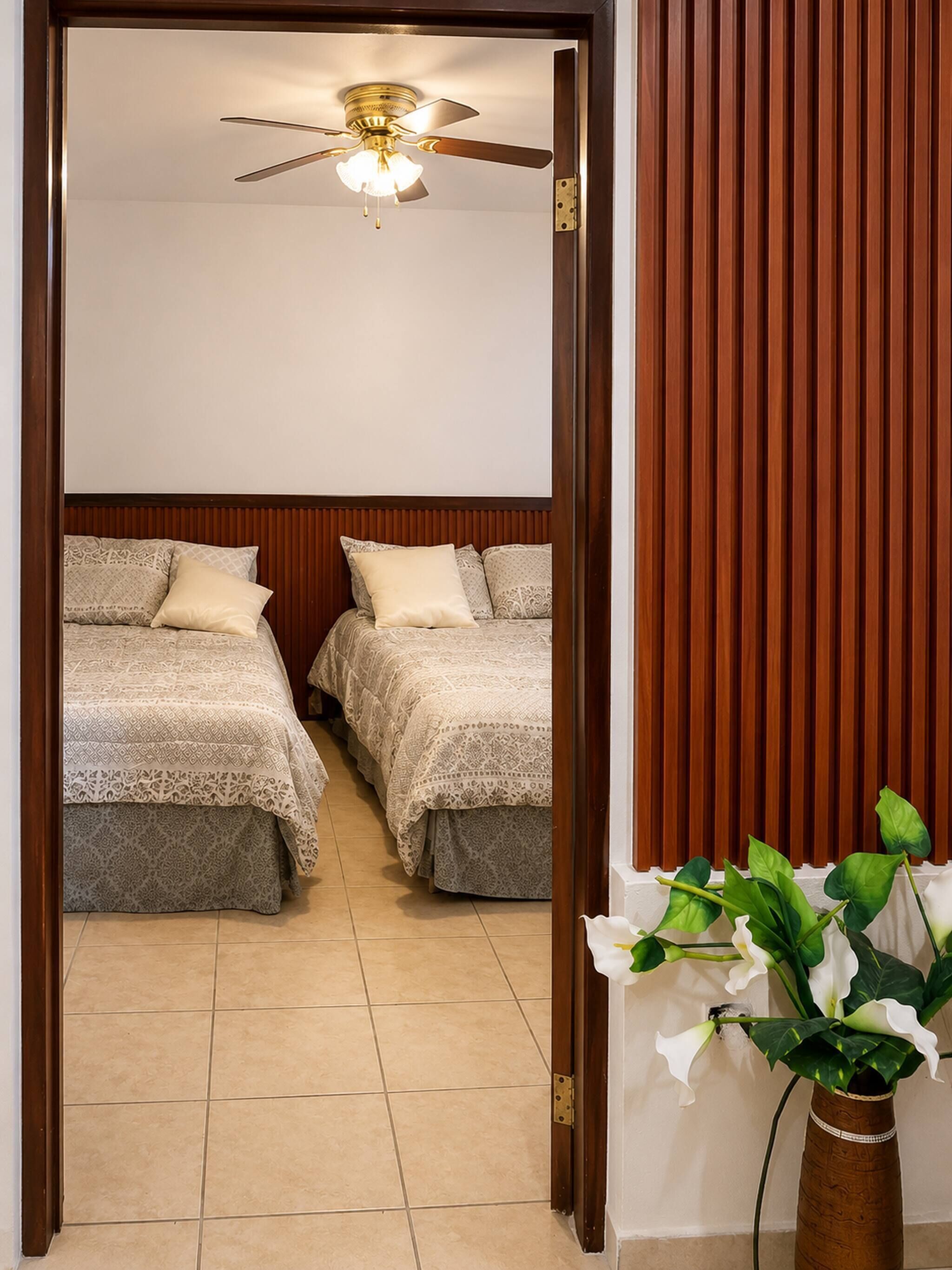 A hotel room with two beds, a ceiling fan, and a potted plant.