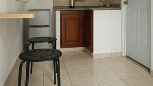 Une cuisine équipée d’un réfrigérateur, d’un évier, d’un placard et d’une porte. Il y a deux tabourets et deux verres à vin sur une table.
