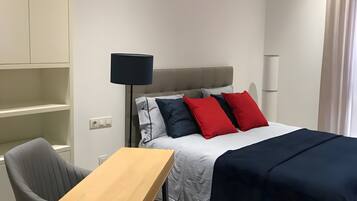 Een hotelkamer met een bed, bureau, stoel, lamp en kledingkast.