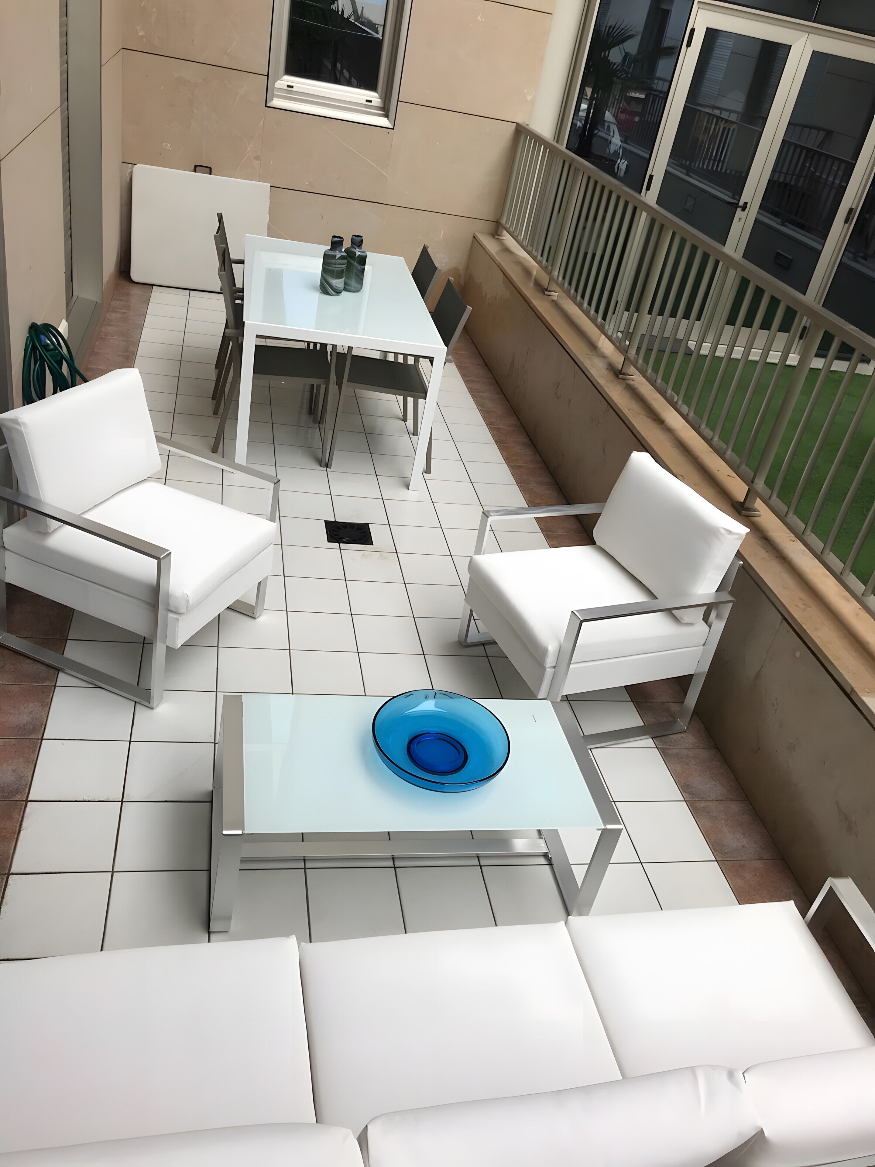 Een balkon met een witte tafel, twee witte stoelen, een blauwe schaal en uitzicht op een gebouw.