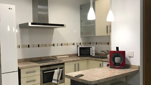 A modern kitchen with a microwave, oven, and a coffee machine. There is a bar stool and a trash bin. - Seafront playa Patacona Mare Nostrum (Alboraya)