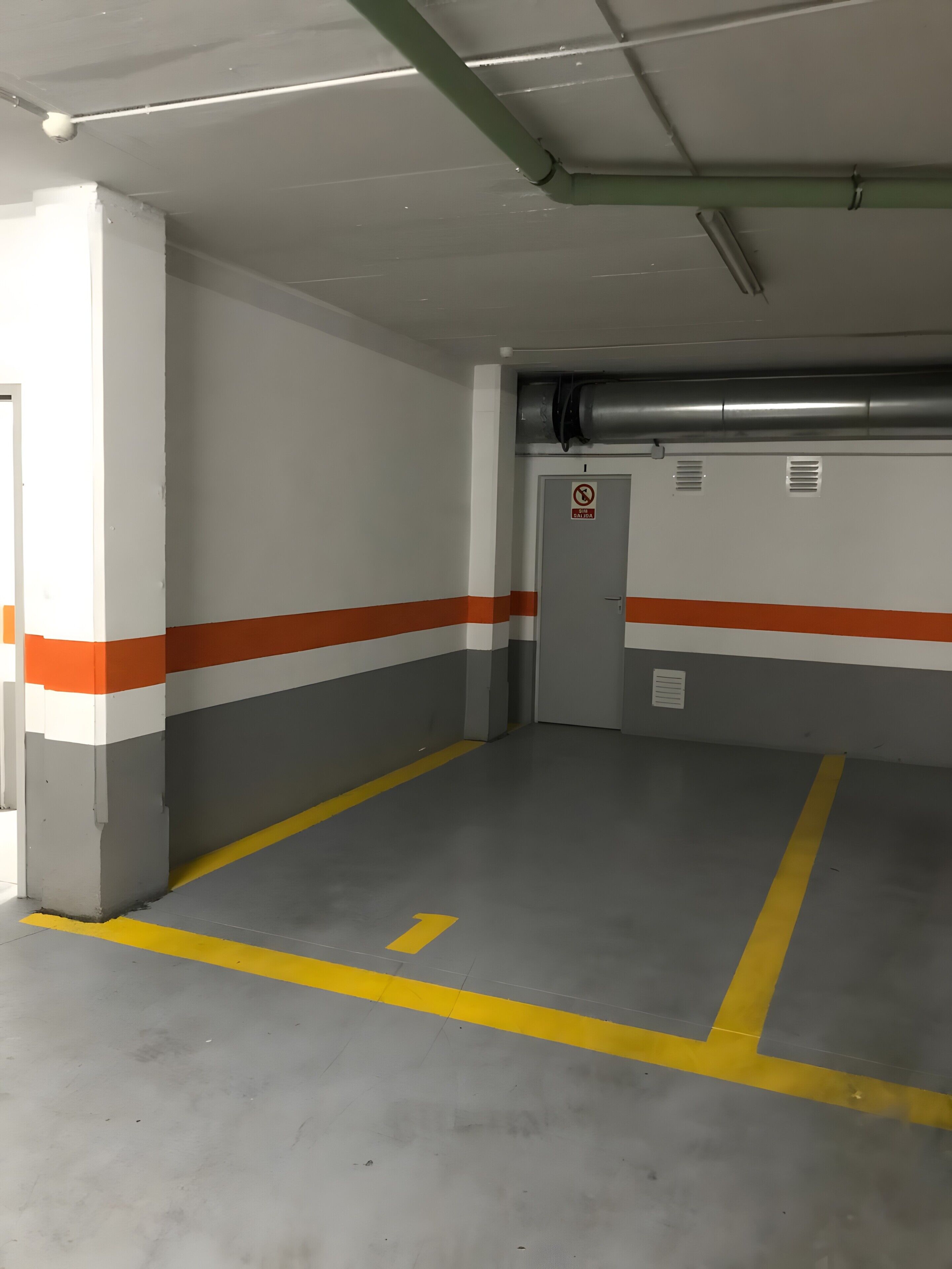 Un garaje para estacionar con espacios delimitados, un letrero de prohibido fumar y conductos de ventilación en el techo.