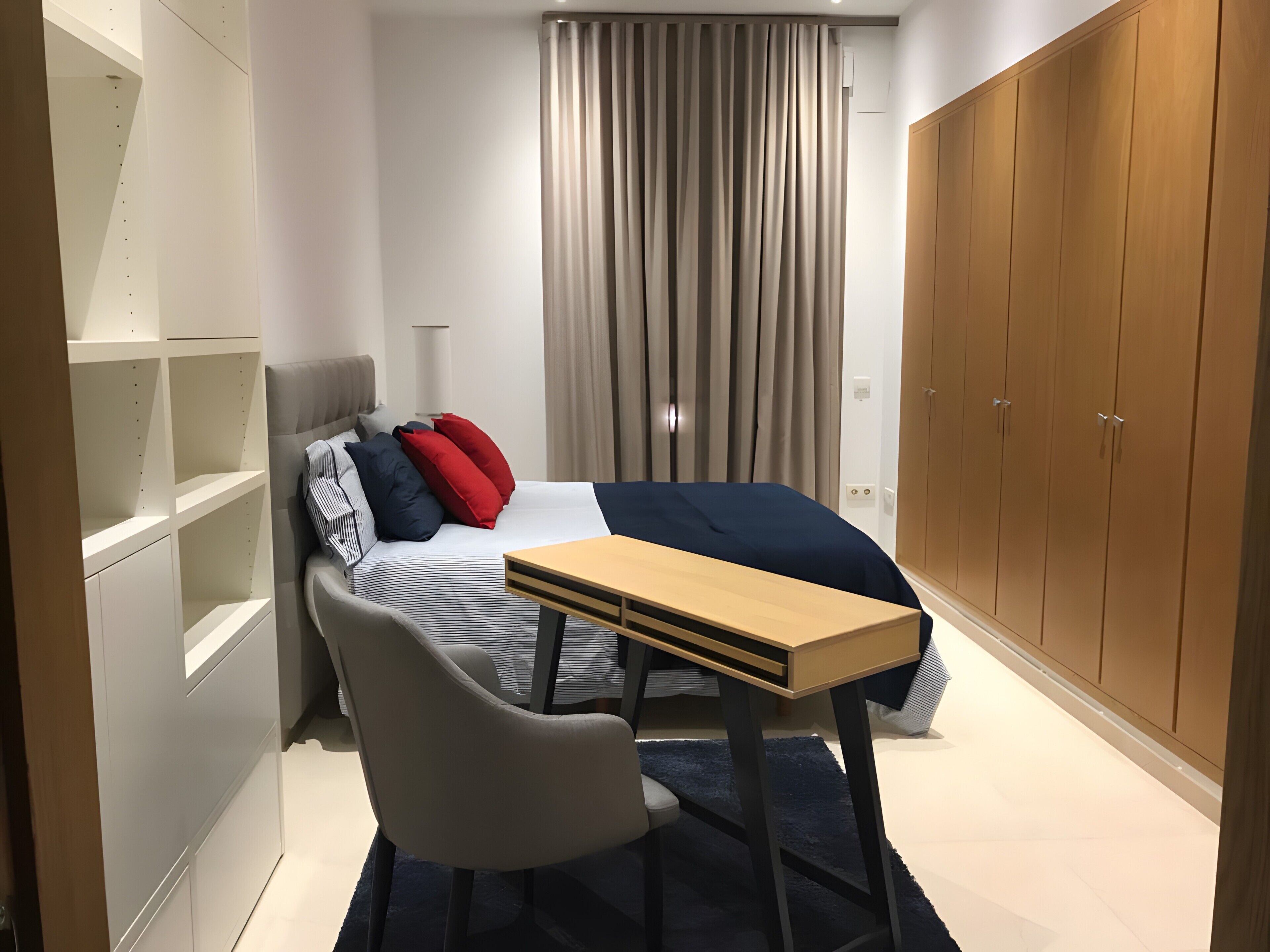Un dormitorio con cama, escritorio, silla, armario y cortina.