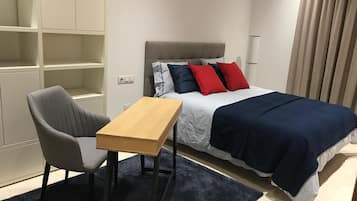 A bedroom with a bed, a desk, a chair, and built-in shelving.