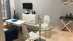A modern living room with a glass dining table, two chairs, a TV mounted on the wall, and a decorative fish wall art piece. - Seafront playa Patacona Mare Nostrum (Alboraya)