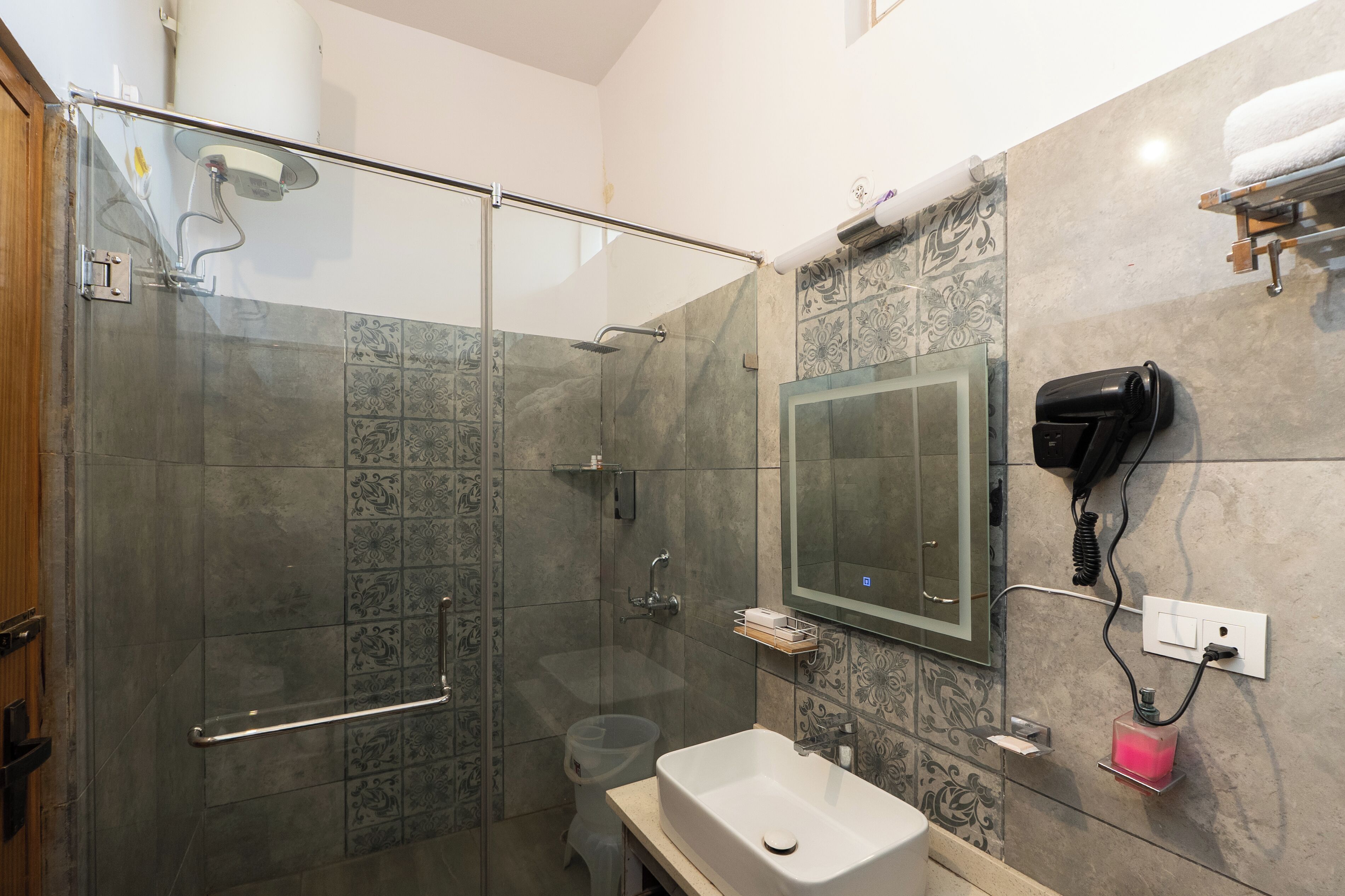 Un baño moderno con cabina de ducha de vidrio, un lavamanos, un secador de pelo y un espejo.